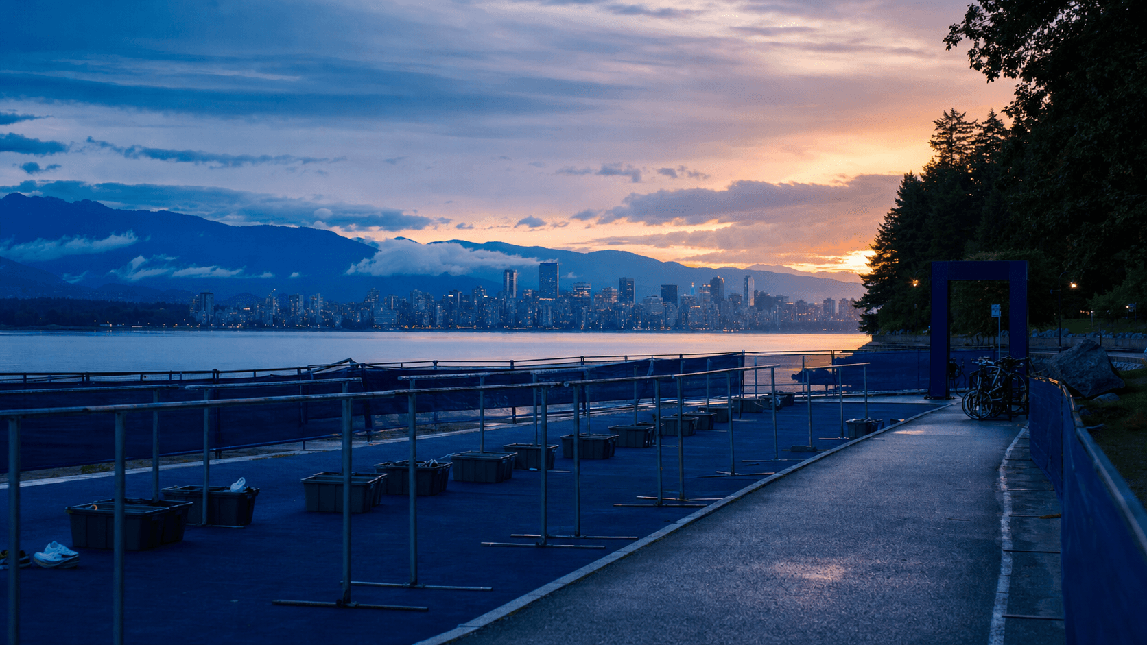 Unbranded Vancouver waterfront triathlon venue with transition racks beside calm Pacific water at dawn