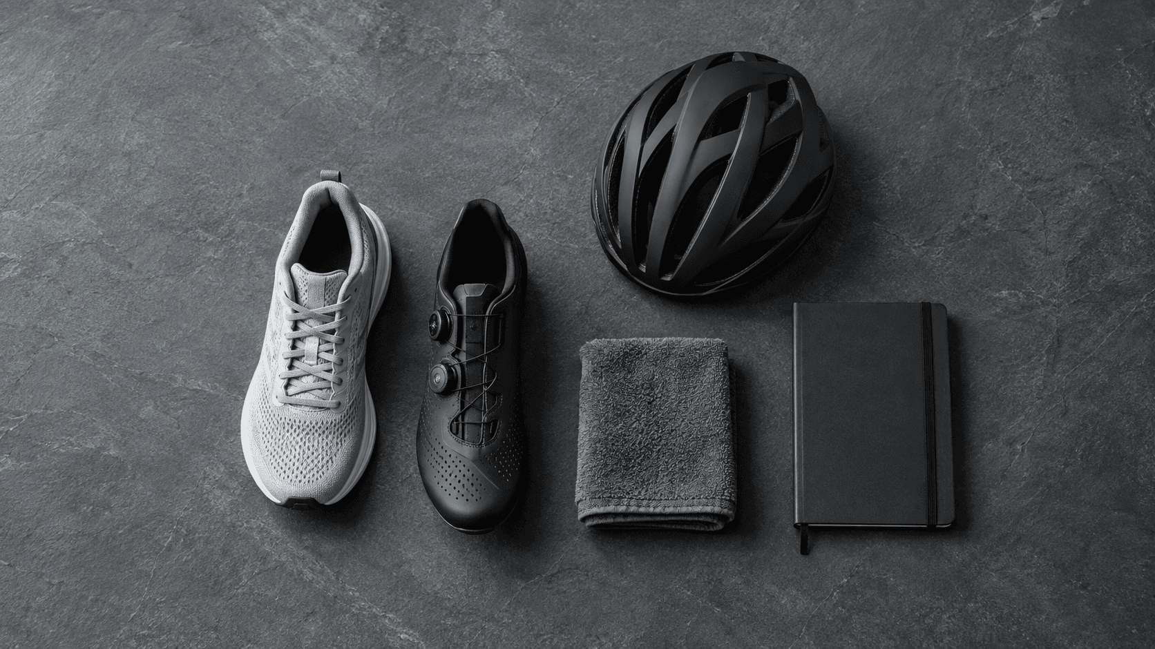 Unbranded running shoe, cycling shoe, helmet, towel and blank training notebook arranged on slate