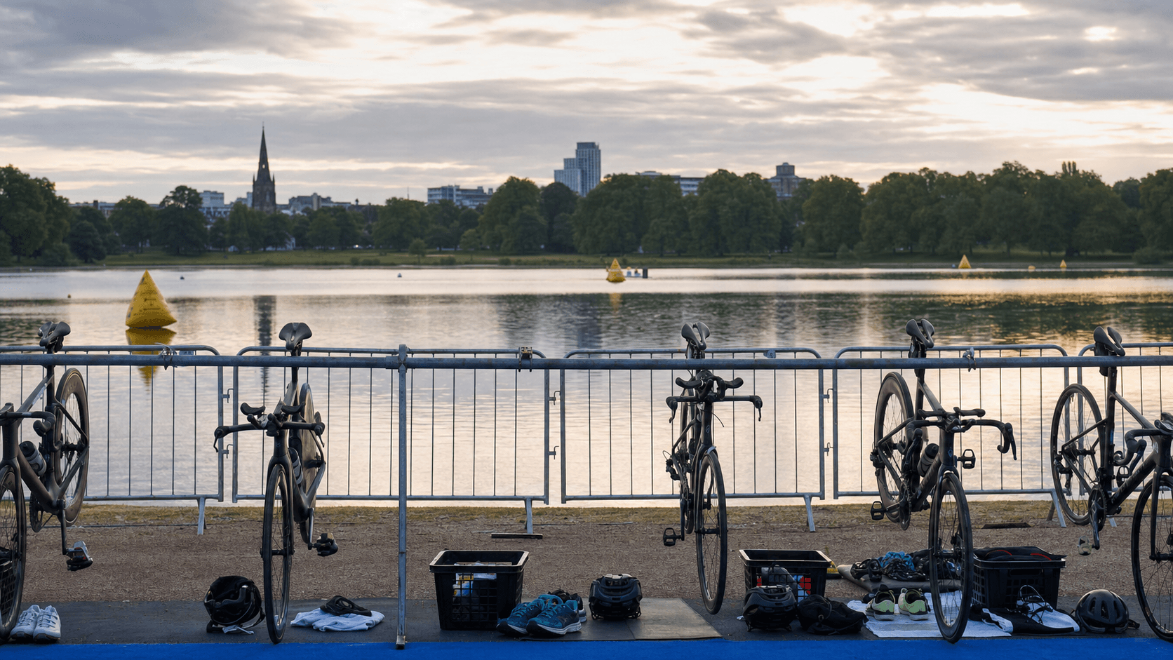 Unbranded triathlon bikes beside a calm lakeside transition area in an English city park